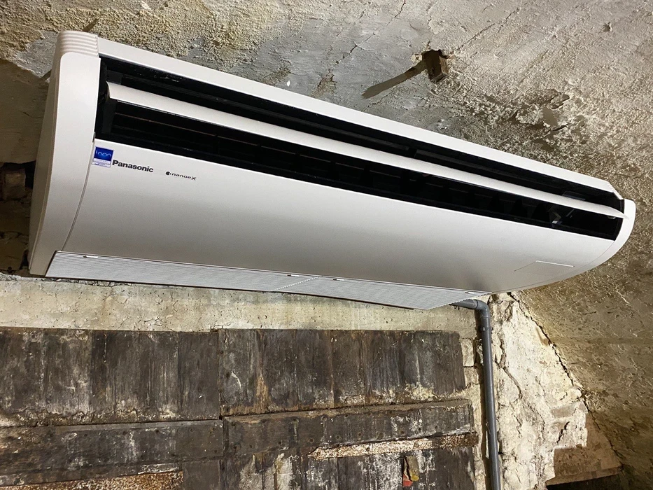 Extérieur résidentiel avec unité de climatisation Hitachi installée sur dalle béton devant maison crépi beige